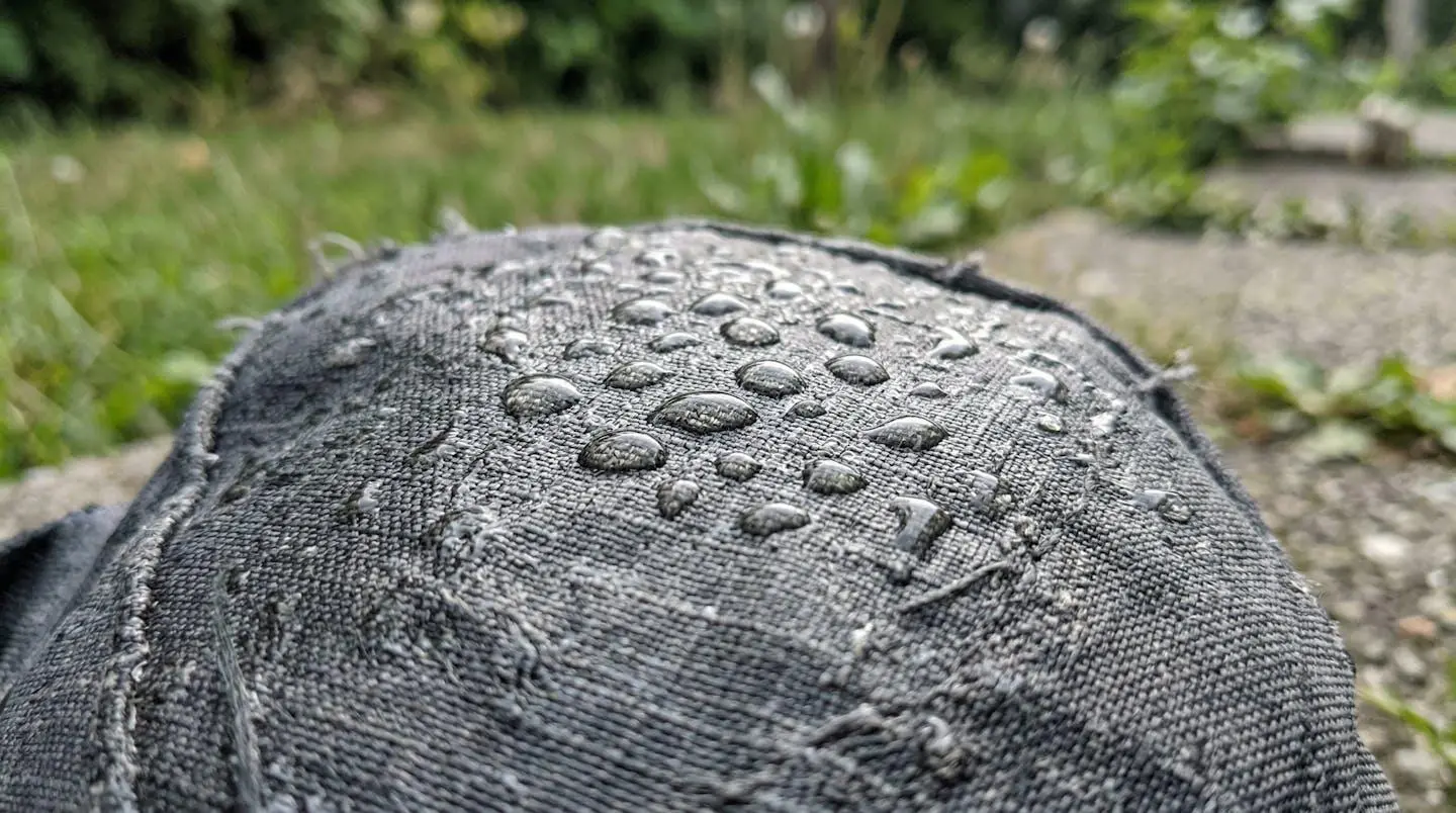 Gros plan sur un tissu technique mouillé avec des gouttelettes d'eau visibles, arrière-plan extérieur flou